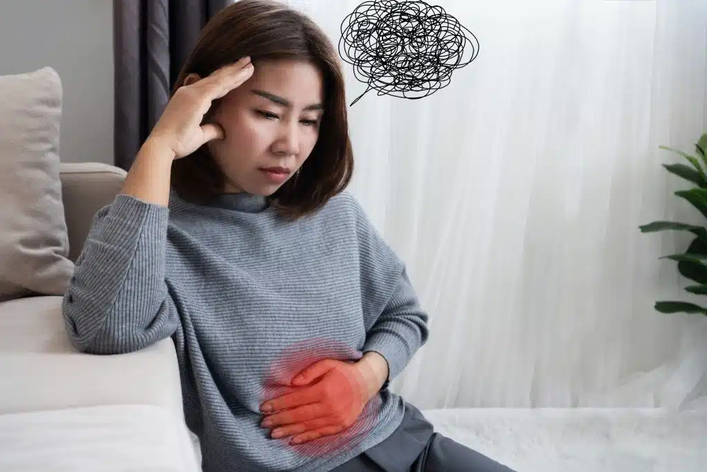 Woman holding stomach with distressed expression, representing the link between gut problems and anxiety or mental distress. Gut-brain connection.
